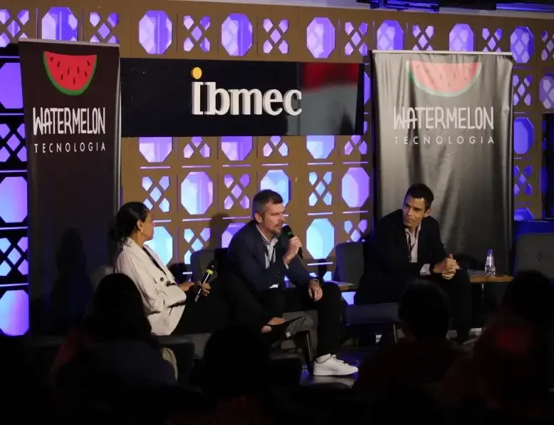 Panel de tres invitados en el escenario, frente a los paneles de Ibmec